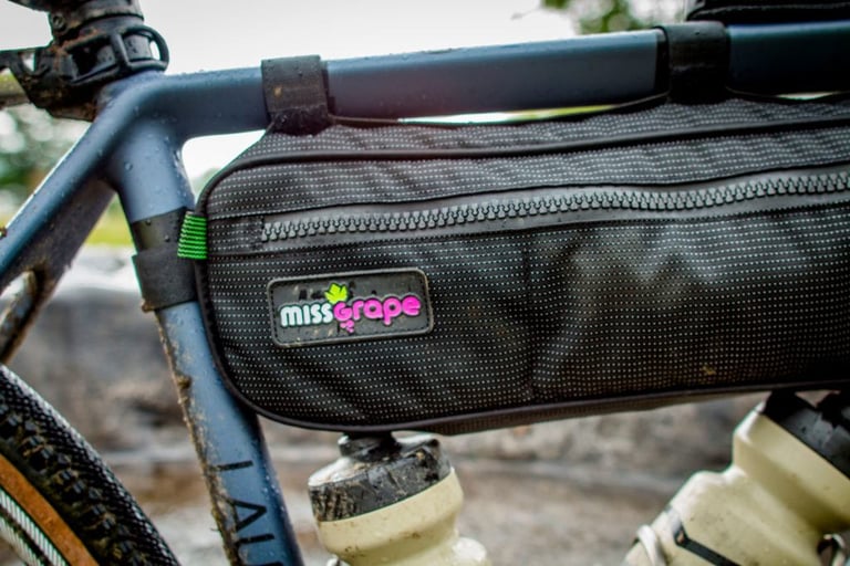 Miss Grape Internode frame bag in the front triangle of the blue Lauf True Grit, spattered with rain and mud.