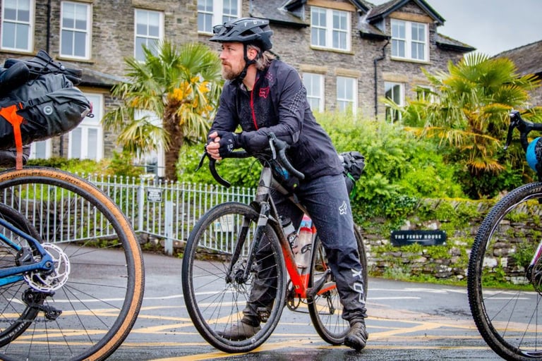 Tristan in Fox kit leans on his gravel bike outside The Ferry House while riders wait for the Windermere ferry.