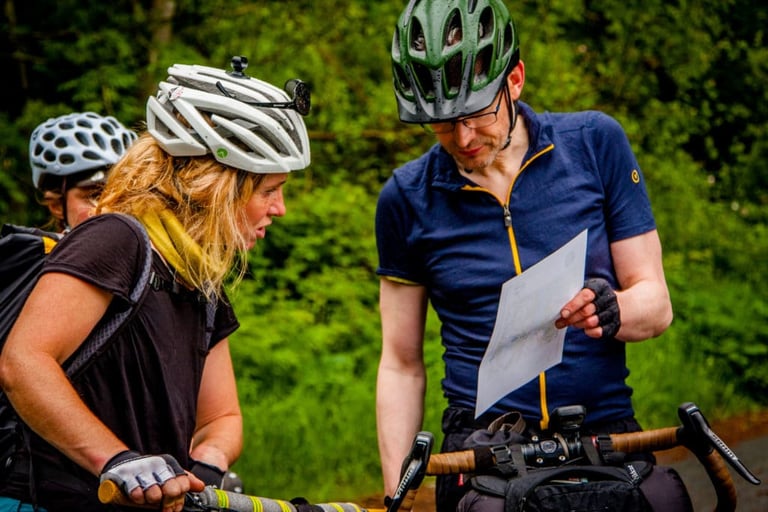 Two riders pore over a printed route map across their handlebars on The Distance bikepacking event.