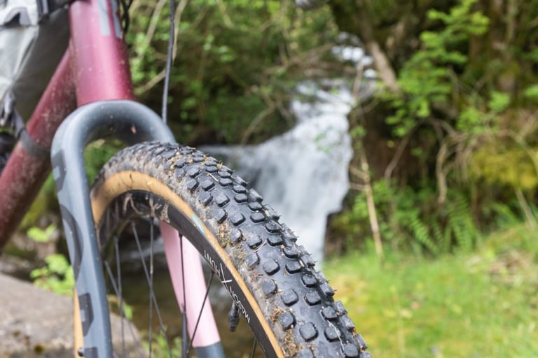 Rene Herse Pumpkin Ridge tyre on the front wheel of a maroon Rondo Ruut AL, with a waterfall blurred behind.