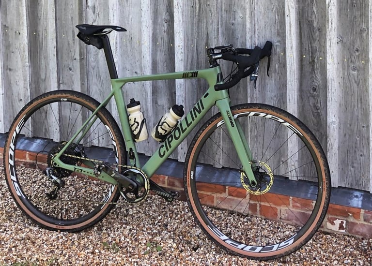 Green Cipollini gravel bike fitted with Scope O2 wheels, leaning against a timber-clad wall.