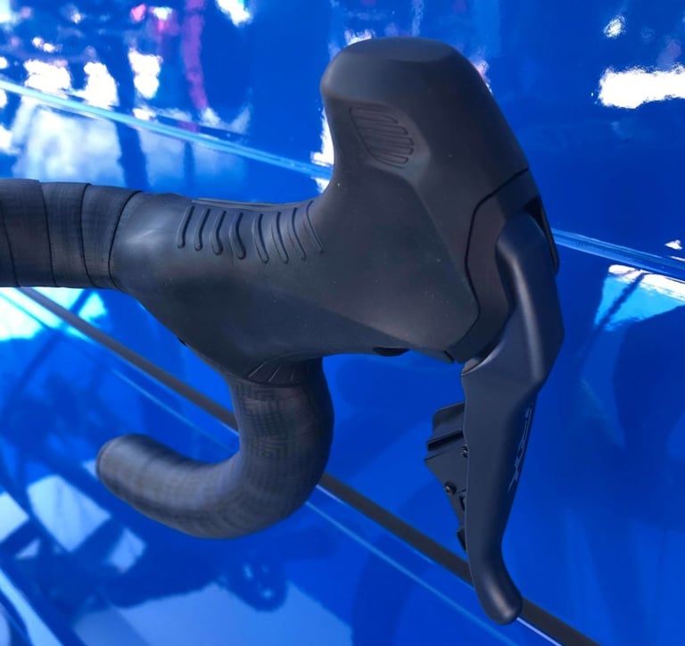Inside view of a Shimano GRX Di2 shifter hood showing the textured non-slip rubber grip, photographed against blue panels.