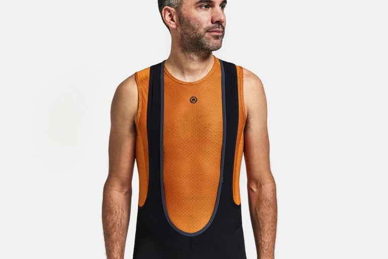 Rider wearing the orange Chapeau mesh sleeveless base layer under black bib shorts.