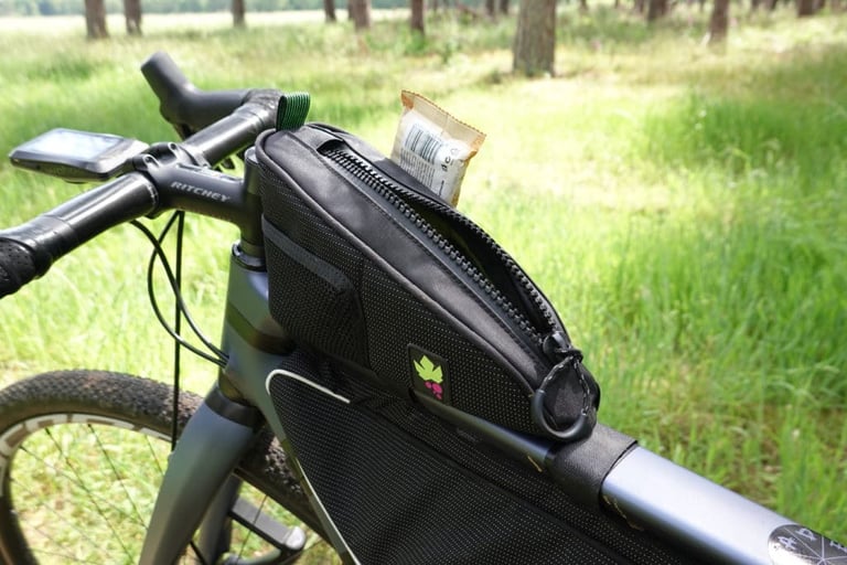 Miss Grape Node 2H top tube bag mounted behind the stem, zip open with an energy bar poking out.