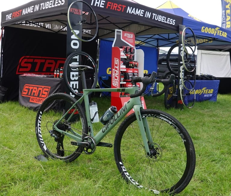 Cipollini MCM All Road displayed on grass in front of Stan's NoTubes and Goodyear tyre tents at an event.