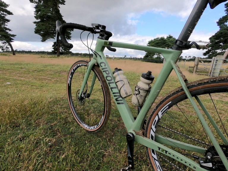 Mud-splattered Cipollini MCM All Road with two bottles, parked in a grassy field after an off-road test ride.