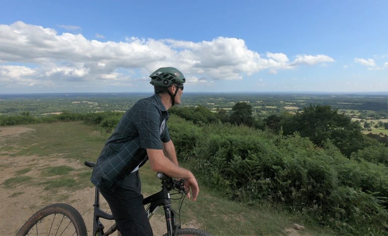 Rider in the Overland shirt pauses on a mountain bike to look out over a wide green view.