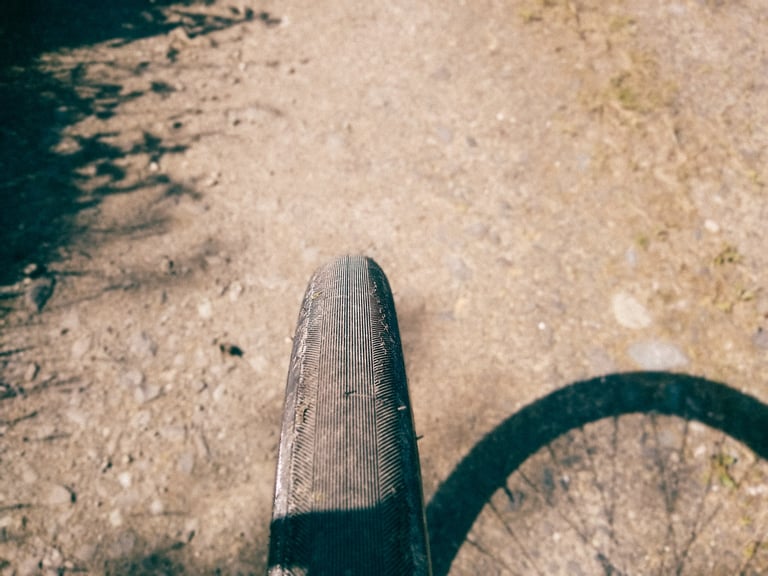 Top view of the Switchback Hill's fine file tread, dusty from the trail, with the wheel's shadow on dry ground.