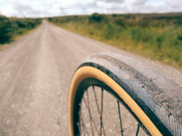 Tan-wall Rene Herse Switchback Hill tyre in close focus on a wide gravel road through open moorland.