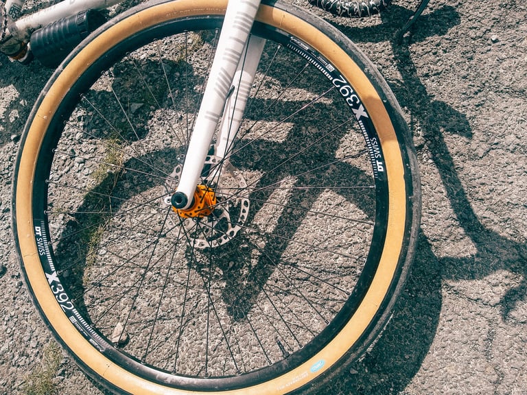 Top-down view of the front wheel, Switchback Hill 650B tyre on a DT Swiss X392 rim with an orange hub, on rough tarmac.