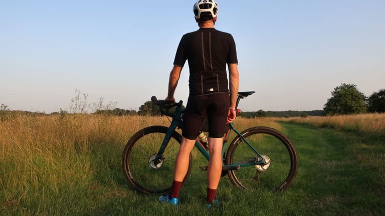 Rear view of the PEdALED Odyssey jersey with reflective strips down the back, rider standing by a gravel bike.