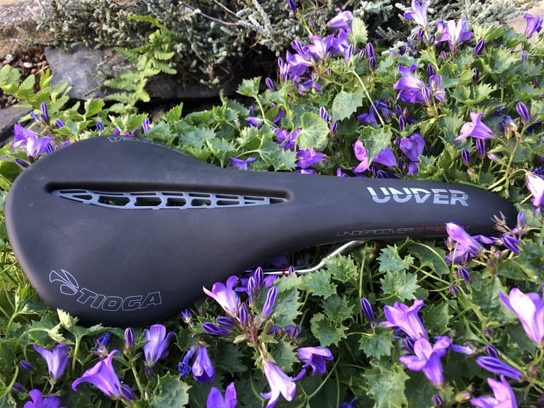 Black Tioga Undercover Stratum saddle, 'Under' lettered on its flank, lying in a bed of purple flowers.
