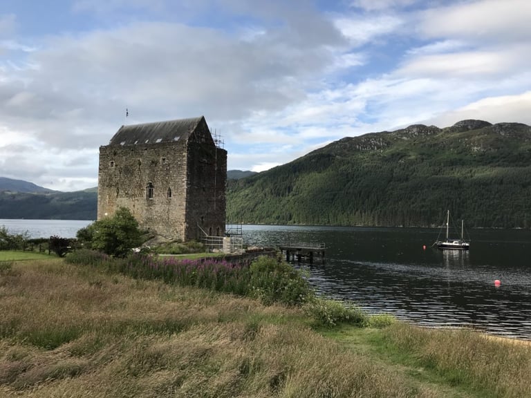 Stone tower house and a moored yacht on a sea loch in Argyll, close to the Dunoon Dirt Dash campsite.