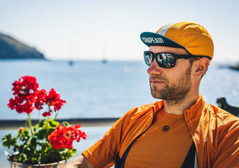 Rider in an orange Chapeau! lightweight cap and sunglasses at a seaside cafe, red geraniums in the foreground.