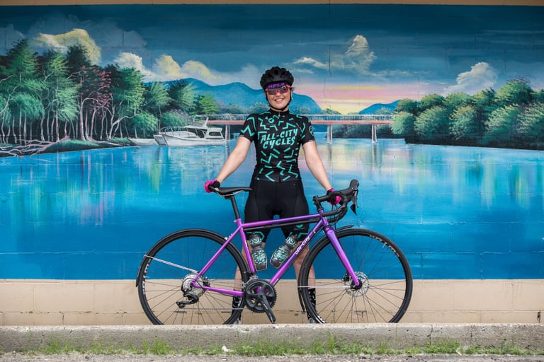 Close view of a rider on an orange-red fade All-City Zig Zag with Whisky wheels and mudguards, a purple bike behind.