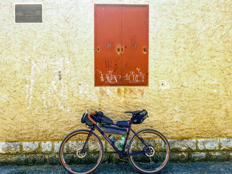 Loaded Velo Orange Piolet leaning on a yellow rendered wall below a red metal shutter covered in graffiti.
