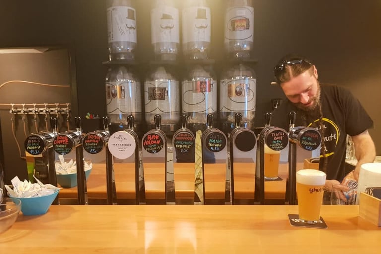 Bartender at a row of craft beer taps in a Koper pub, with a glass of beer on the bar.