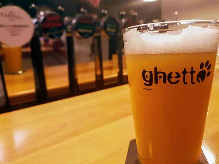 Glass of pale craft beer branded Ghetto on a pub bar, with beer taps blurred behind.