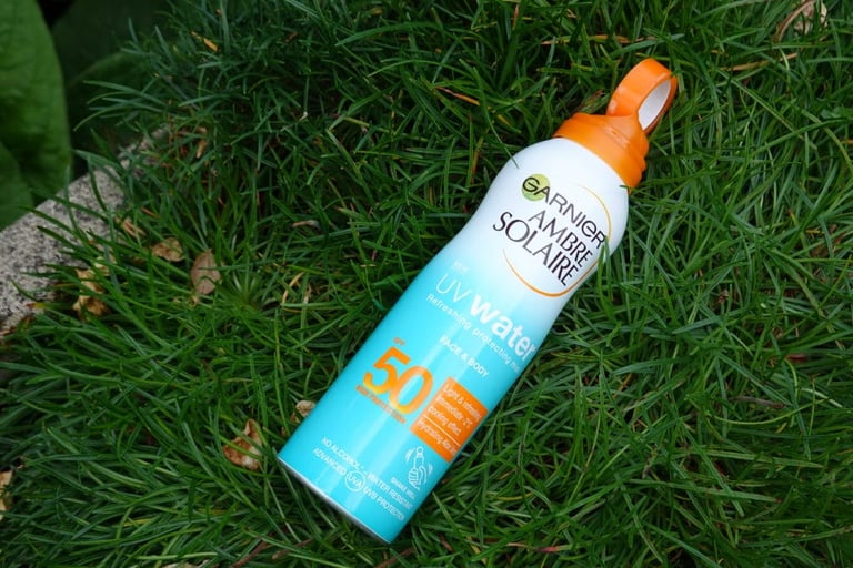 Garnier Ambre Solaire UV Water SPF50 sun protection mist spray lying in grass.