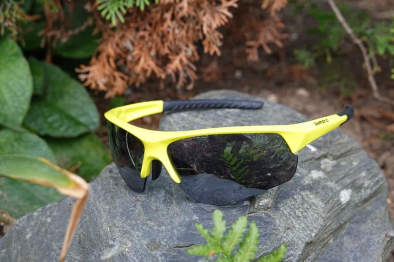 Shimano Twinspark cycling glasses with bright yellow frames and dark mirrored lenses, resting on a rock.