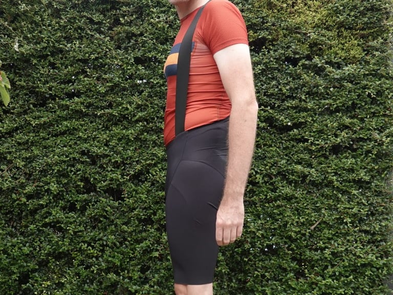 Side view of the 7mesh MK3 Bib Short showing the low-cut front and shoulder strap, worn with an orange jersey.