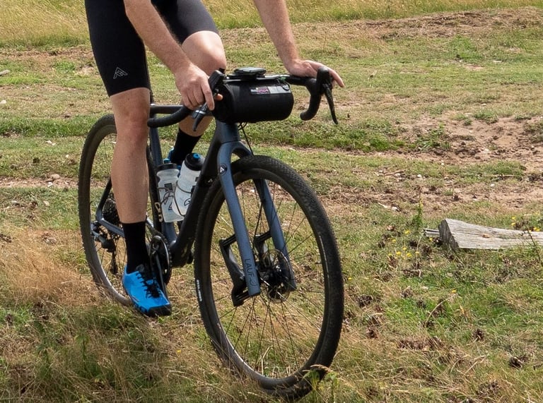 Rider on a Lauf gravel bike with the Miss Grape Moon bar bag fitted, riding over rough grass.