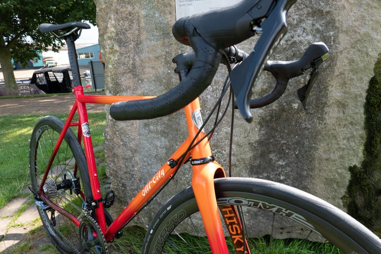 Close view of the Zig Zag's cockpit, head tube and orange fork with Whisky decal, leaning against a stone marker.