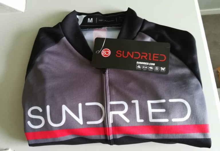 Folded Sundried Peloton short sleeve training jersey in grey, black and red, with the hang tag attached.
