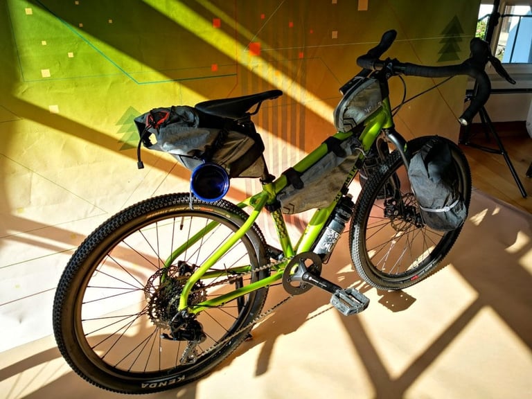 Bombtrack Beyond Junior in green, three-quarter view from the drive side with bikepacking bags fitted.