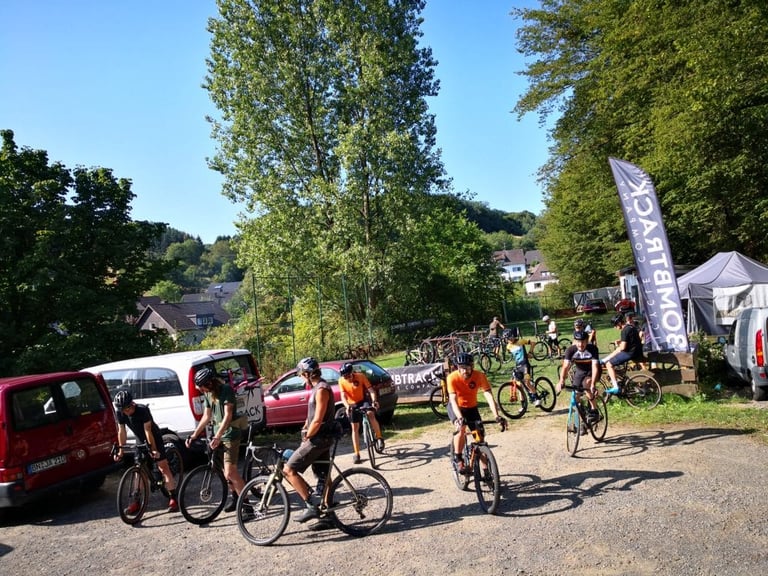 Riders in helmets gather on bikes in a gravel car park beside a Bombtrack flag before the Groundwork ride.