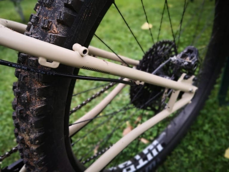 Rear triangle of the Bombtrack Cale with a wide tyre, rack mounts on the seatstay and a Magura brake hose.