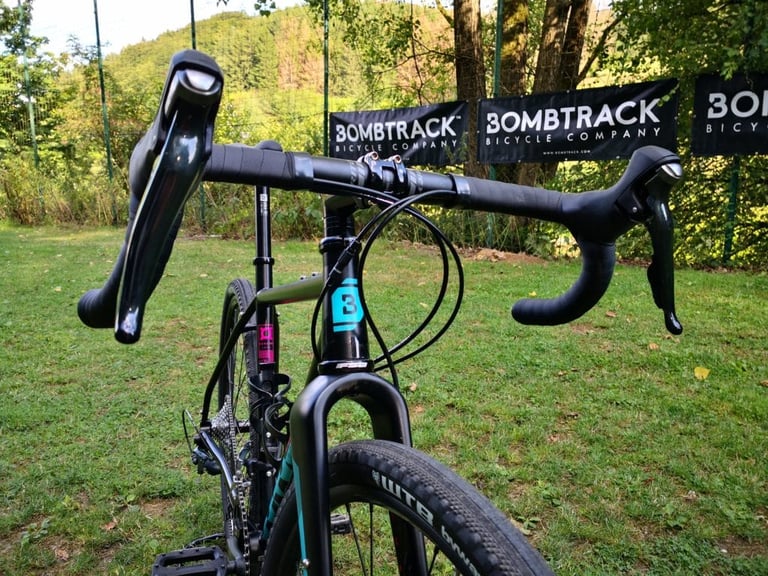Drop bars, brake levers and teal fork of the Bombtrack Hook WMN seen from the front, with Bombtrack banners behind.