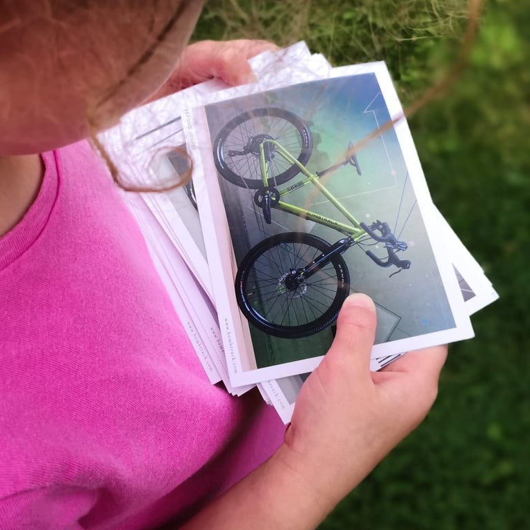 Child in a pink top holds a stack of Bombtrack 2020 postcards, the top one showing the Beyond Junior.