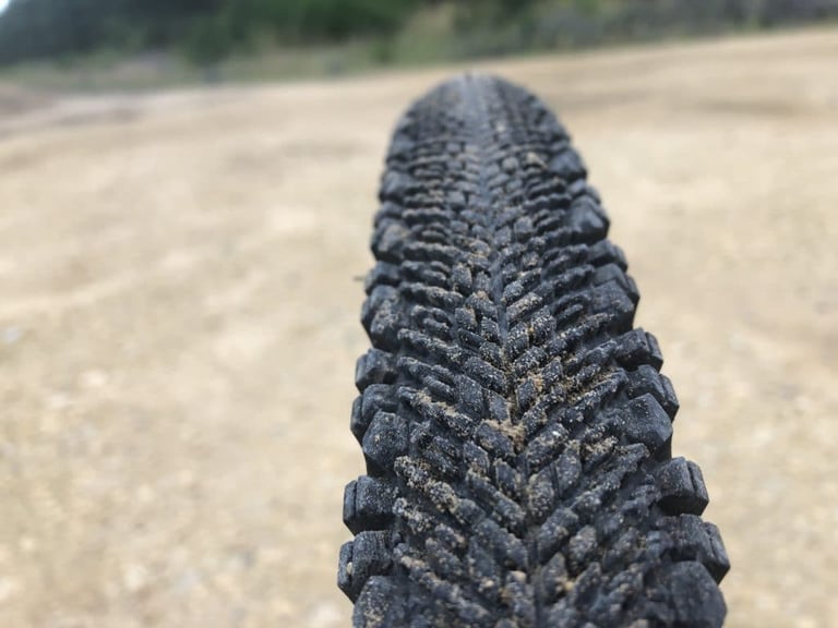 Close-up of the WTB Venture 40 tread, its chevron ridges packed with dry sand on a gravel track.