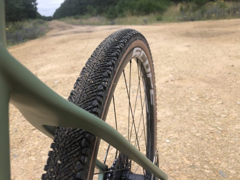 WTB Venture 40 on a Scope O2 rim beside the green frame of a gravel bike, on a pale gravel forest track.