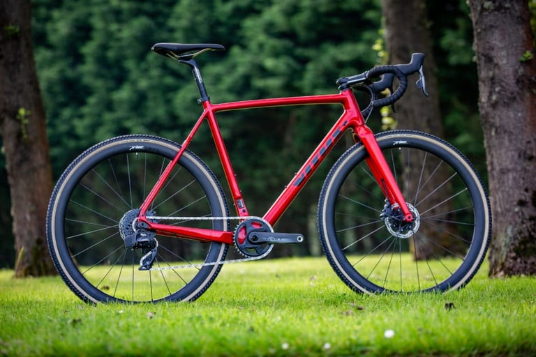 Glossy red Vitus Energie CRX eTap with Prime carbon wheels and tan-wall tyres, side view in front of dark conifers.