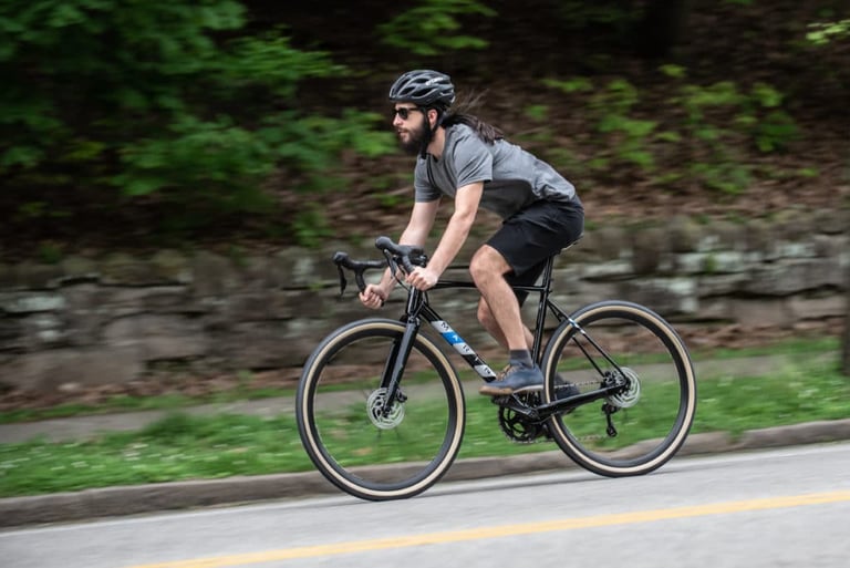 Rider on the black Marin Lombard with tan-wall tyres on a road beside a stone wall and trees.