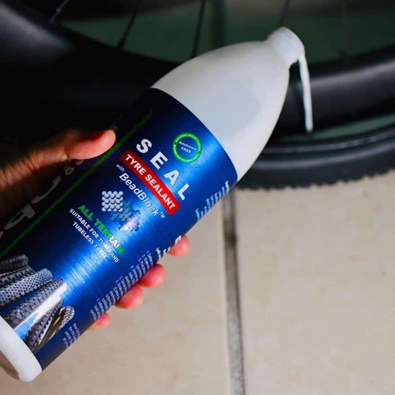 Hand holding a bottle of Squirt SEAL tyre sealant over a tyre, with a drip running from the neck.