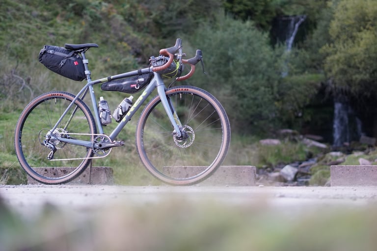 Side view of the Trek Crockett 7 with Alpkit seat pack, frame bag and bar bag, two bottles and a waterfall behind.