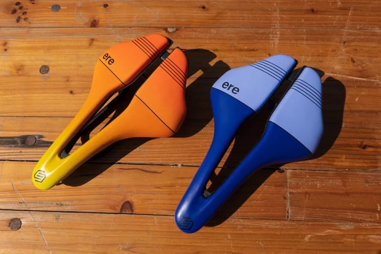 ERE Research Genus saddles in orange-to-yellow and blue-and-lilac colourways on a wooden table.