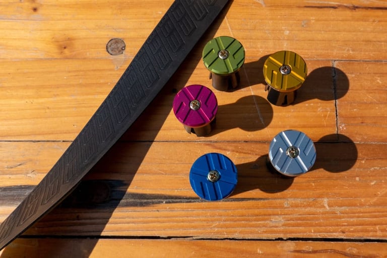 ERE Research Explorator bar tape beside five anodised CNC aluminium bar end plugs in green, gold, pink, blue and silver.