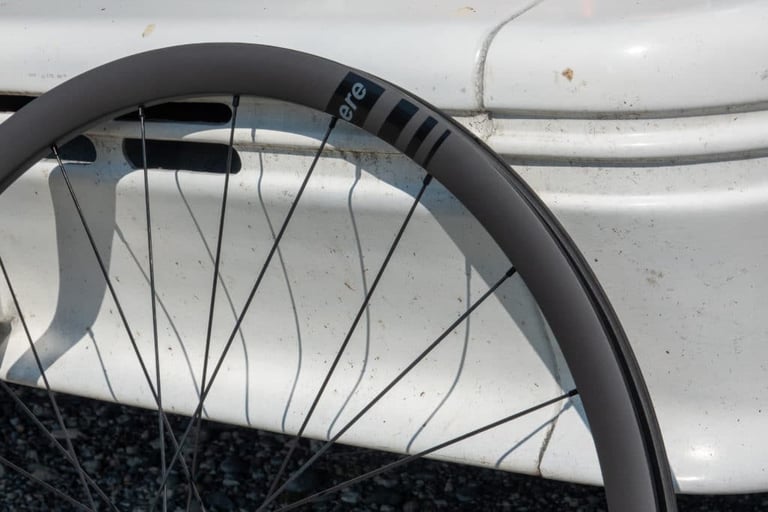 Close-up of the ERE Genus SL 30 carbon rim and spokes with the logo decal, leaning on a white van.