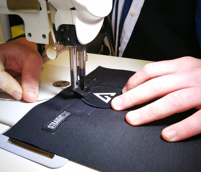 Sewing machine stitching a round logo patch onto the black Cordura panel of the bar bag, beside its woven label.