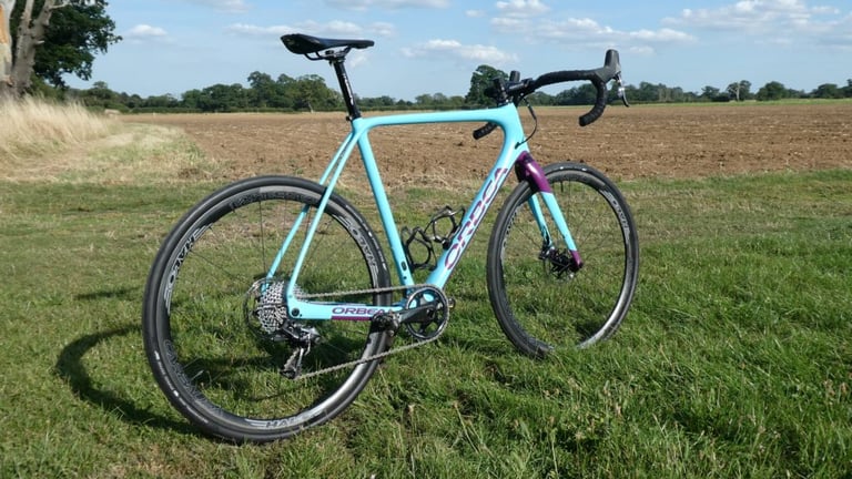 Rear three-quarter view of the Orbea Terra on Halo Carbaura wheels, parked on grass beside a ploughed field.