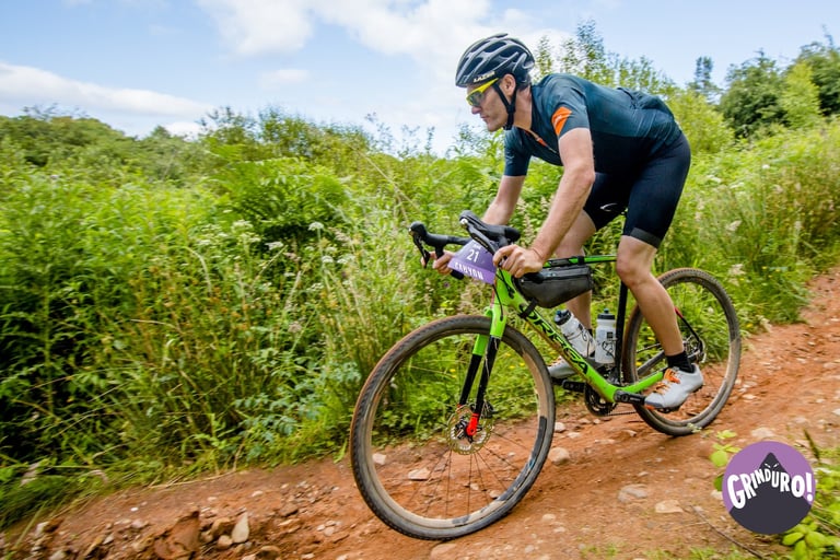 Grinduro Scotland 2019 rider on a green gravel bike rides a red dirt track between bushes on the Isle of Arran.