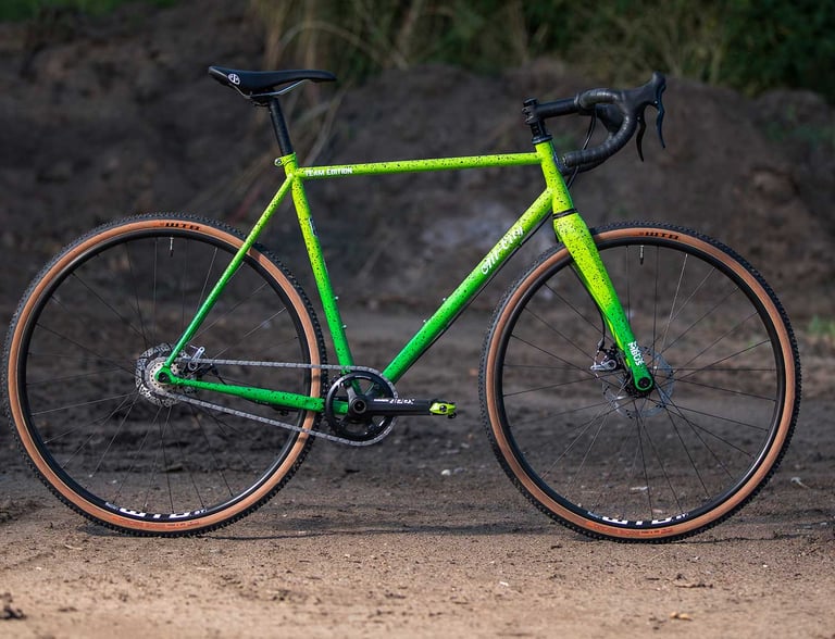 All-City Nature Boy 2020 in fluro green splatter paint with Team Edition decals, side view on a dirt track.
