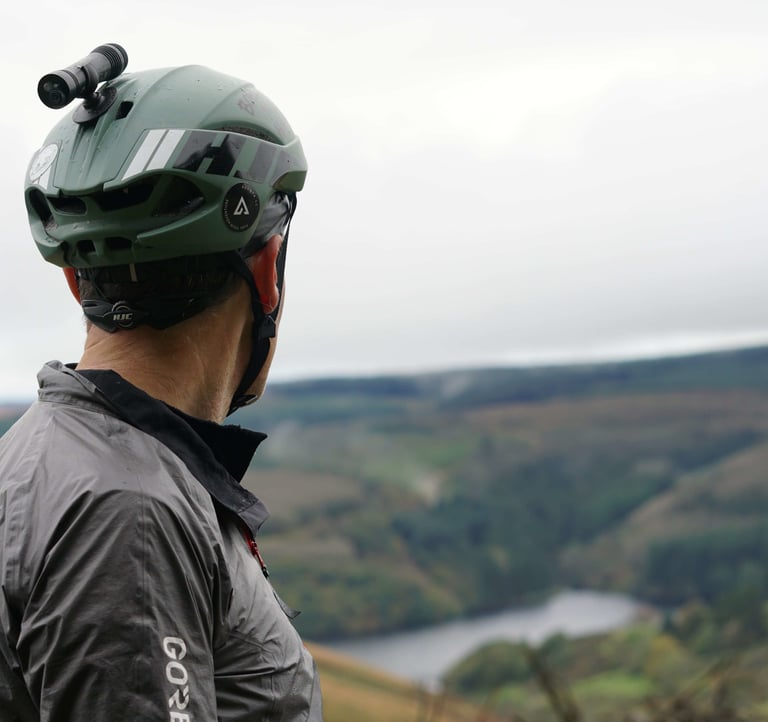 Rider with a helmet-mounted light looks out over a reservoir valley in the Elenydd, Mid Wales, on the Wildcat 100 ride.