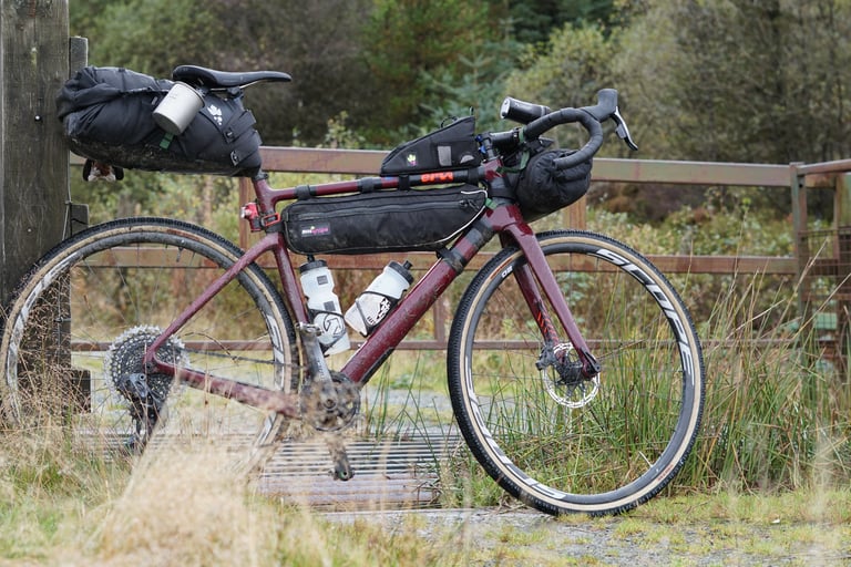 Cervelo Aspero loaded with saddle pack, frame bag and bar bag for bikepacking, leaning against a wooden gate post.