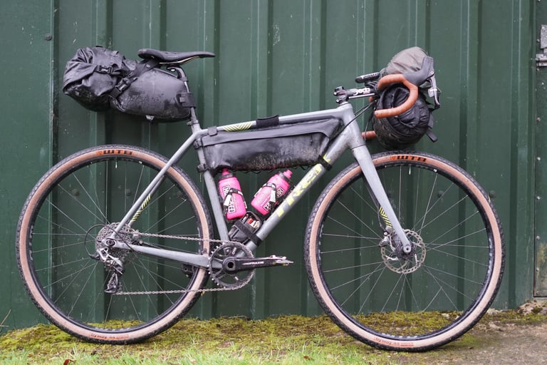 Trek Crockett cyclocross bike with frame bag, seat pack and bar roll, leaning on a green shed before the Wildcat 100 ride.