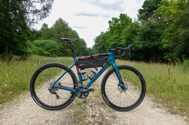 Wilier Jena with a frame bag and two bottles on Hunt 700c wheels, standing on a chalky gravel track between trees.